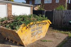 Large skip filled with conifer branches and garden waste on the driveway